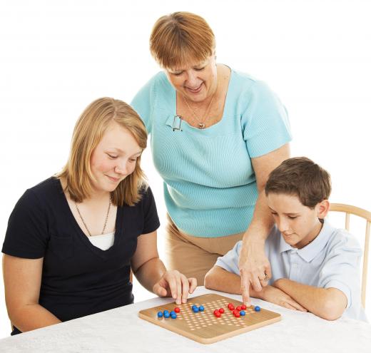 Families enjoy playing Chinese checkers with adults offering assistance to younger players.